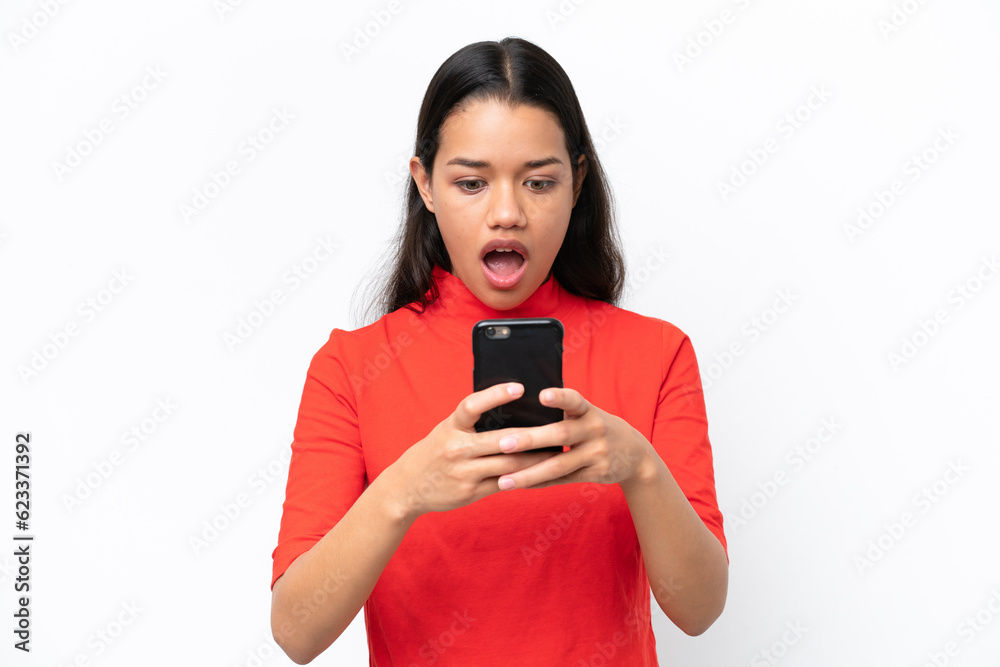 Young Colombian woman isolated on white background looking at the camera while using the mobile with surprised expression Young Colombian woman isolated on white background looking at the camera while using the mobile with surprised expression