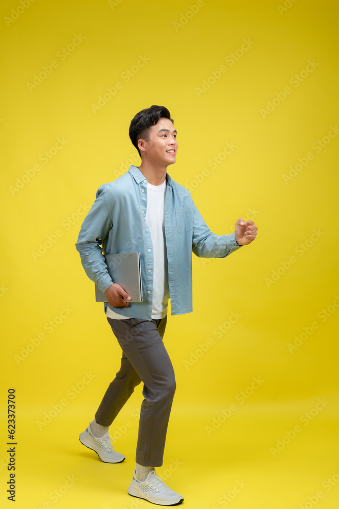 Φωτογραφία Portrait of young man holding laptop, studio shot on yellow background