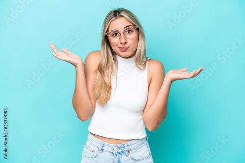 Young caucasian woman isolated on blue background having doubts while raising hands