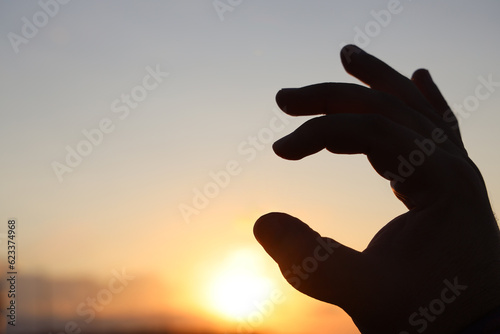 mockup. male hand holding something between fingers on yellow sunset sky background. mock up backdrop.