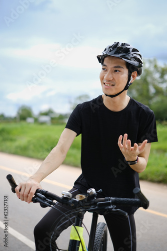 Happy asian man cyclist speaking on phone through earphones while having break during cycling bike in the park