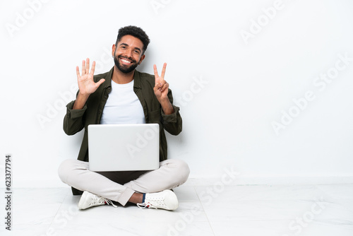 Young Brazilian man with a laptop sitting on the floor isolated on white counting seven with fingers photo