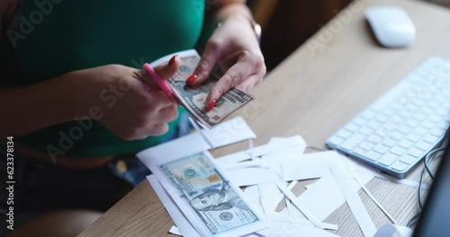 A woman sitting at a table cuts out fake dollars with scissors, close-up. Counterfeit money, fraud crime