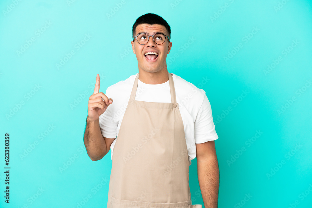 Restaurant waiter man over isolated blue background pointing up and surprised Restaurant waiter man over isolated blue background pointing up and surprised