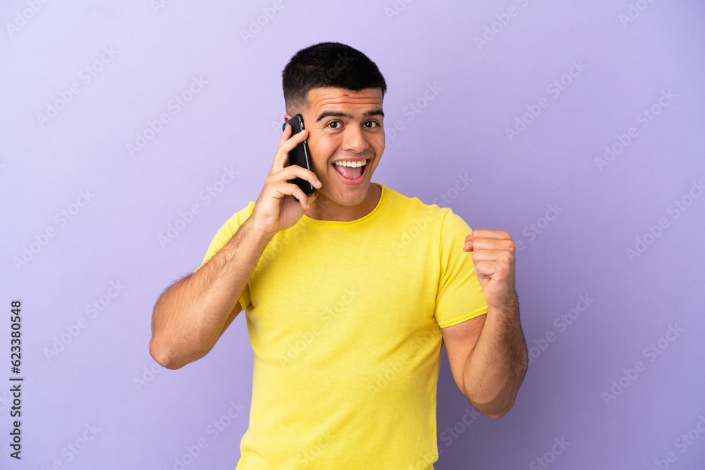 Young handsome man using mobile phone over isolated purple background celebrating a victory in winner position Young handsome man using mobile phone over isolated purple background celebrating a victory in winner position