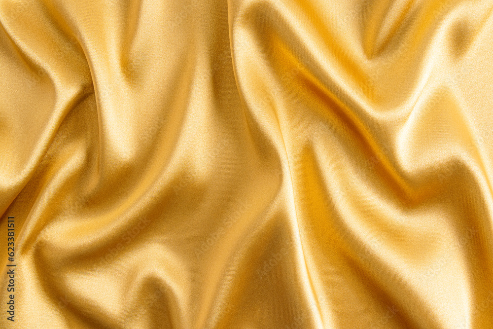 Fototapeta premium Elegant satin fabric with a golden color. The luxurious texture of the soft folds of the fabric. The concept of a festive background. design.