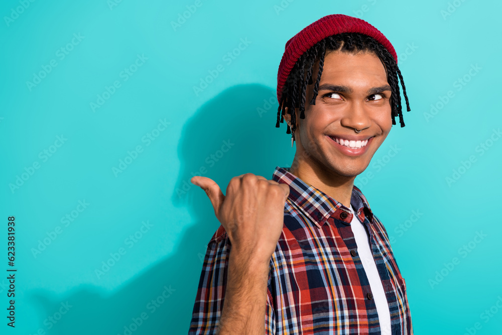 Fototapeta premium Photo of pleasant cheerful guy with cornrows dressed checkered shirt directing look at offer empty space isolated on teal color background