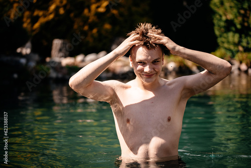 A young handsome guy comes out of a transparent pond on a sunny and hot day after a long swim