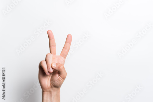 Close-up of a man's hand showing gesture number two or victory on a white background.