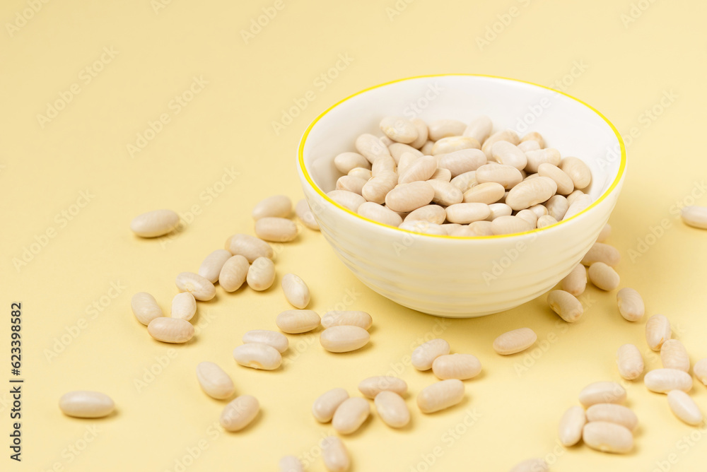 White beans in white bowl and scattered on a beige or yellow background top view White beans in white bowl and scattered on a beige or yellow background top view
