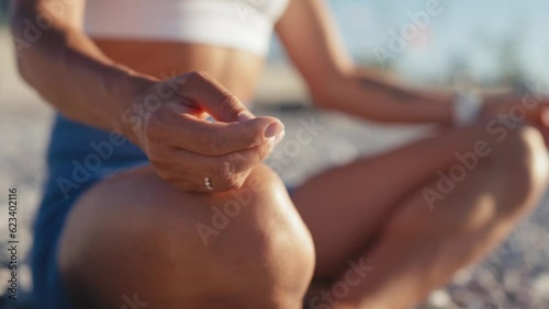 Woman with short hair sitting in lotus position doing yoga exercise meditating on beautiful beach . Girl on holidays sitting on seaside on cloudy day. High quality 4k footage