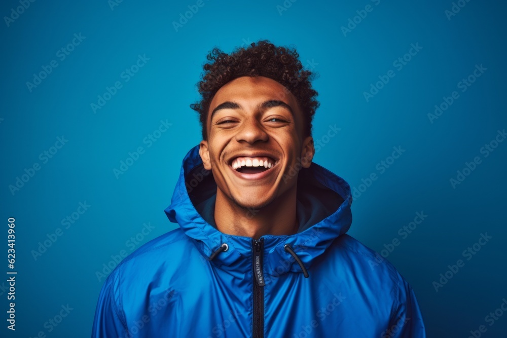 Lifestyle portrait photography of a happy boy in his 20s wearing a lightweight windbreaker against a royal blue background. With generative AI technology Lifestyle portrait photography of a happy boy in his 20s wearing a lightweight windbreaker against a royal blue background. With generative AI technology