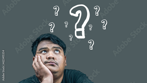 Fotografie Asian young man sitting and wondering There is a question mark symbol on a gray background