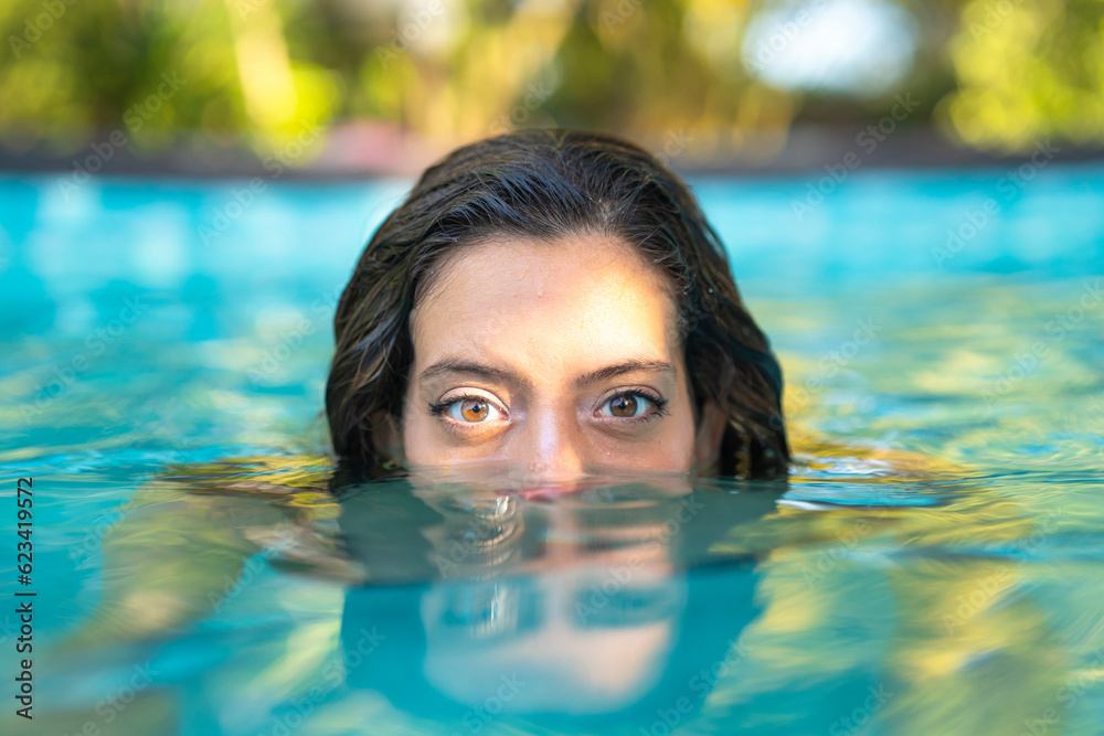 Beautiful woman immersing in water in a private swimming pool looking at camera