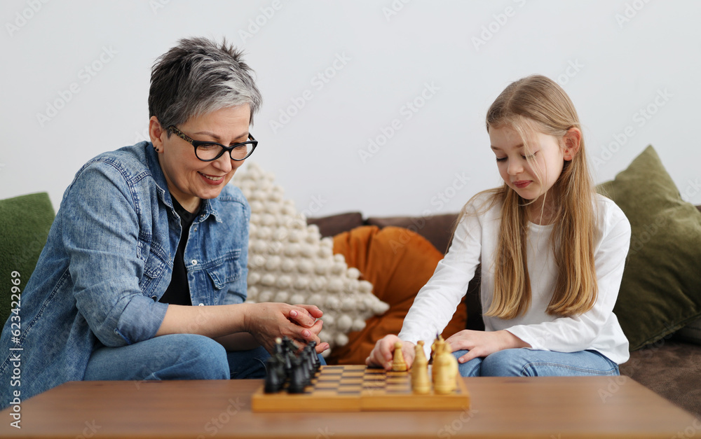 Fototapeta premium Happy grandmother and granddaughter play chess on the sofa.