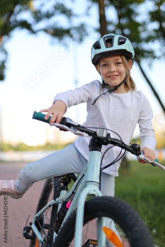Cheerful girl rides a bicycle in a helmet along the bike path in the park. © Andrii Zastrozhnov