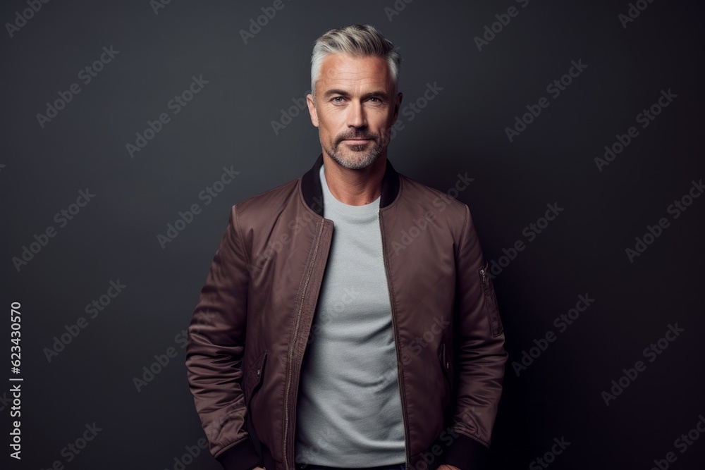 Lifestyle portrait photography of a tender mature man wearing a sleek bomber jacket against a dark grey background. With generative AI technology