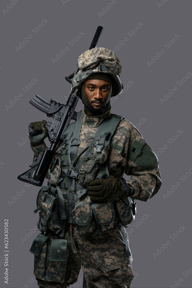 Confident soldier in NATO uniform and helmet poses with his rifle on a plain grey background, showcasing the courage and strength of military personnel Confident soldier in NATO uniform and helmet poses with his rifle on a plain grey background, showcasing the courage and strength of military personnel