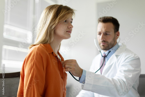 Focused man cardiologist or general practitioner in white coat listening heartbeat or young female patient at checkup meeting, preventing cardiovascular disease photo