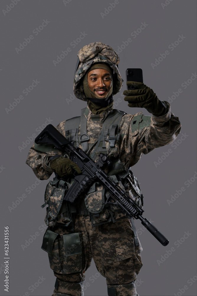 Happy military man in uniform and helmet takes a selfie or video chats on his smartphone, exhibiting the tech skills and positivity of soldiers in uniform