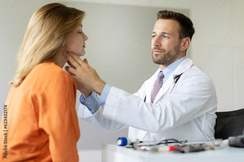 Professional male doctor examining thyroid gland of female patient during checkup in private clinic, sitting at desk in hospital office Professional male doctor examining thyroid gland of female patient during checkup in private clinic, sitting at desk in hospital office