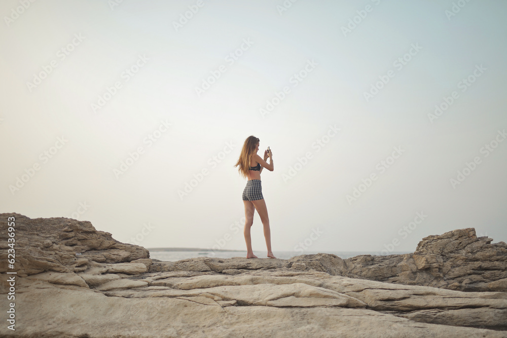 full length of woman's back with a smartphone in her hand at a beach