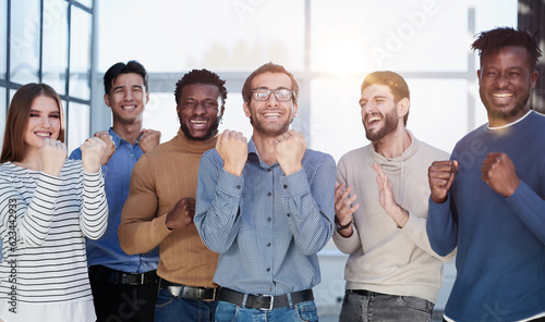 Group of happy managers rejoice at a successful deal by clenching their hands into fists and raising them up