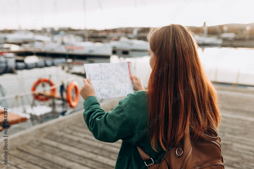 Happy tourist girl with map travels in Europe. Vacation concept by exploring interesting places to travel by rented boat or yacht. Woman Searching locations, walking along the waterfront, seaside.