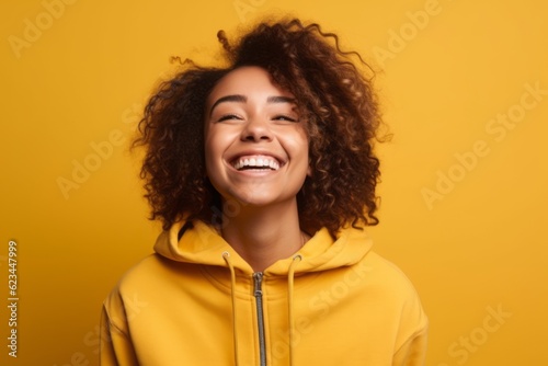 Medium shot portrait photography of a grinning girl in her 30s wearing a cozy zip-up hoodie against a yellow background. With generative AI technology