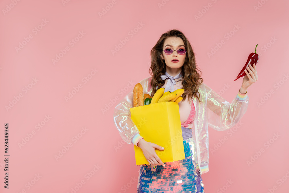 housewife concept, attractive young woman in sunglasses carrying paper bag with groceries and holding red pepper, posing like a doll on pink background, conceptual photography, home duties housewife concept, attractive young woman in sunglasses carrying paper bag with groceries and holding red pepper, posing like a doll on pink background, conceptual photography, home duties