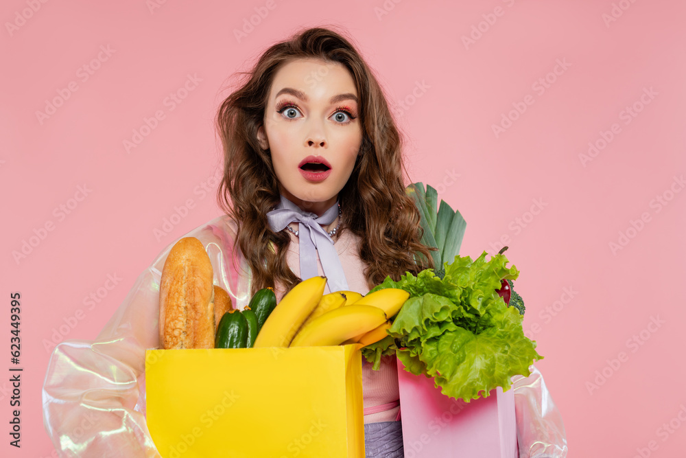 housewife concept, shocked young woman carrying grocery bags with vegetables and bananas, model with wavy hair on pink background, conceptual photography, home duties, stylish wife housewife concept, shocked young woman carrying grocery bags with vegetables and bananas, model with wavy hair on pink background, conceptual photography, home duties, stylish wife