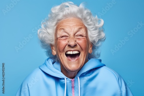 Headshot portrait photography of a happy old woman wearing a comfortable tracksuit against a periwinkle blue background. With generative AI technology
