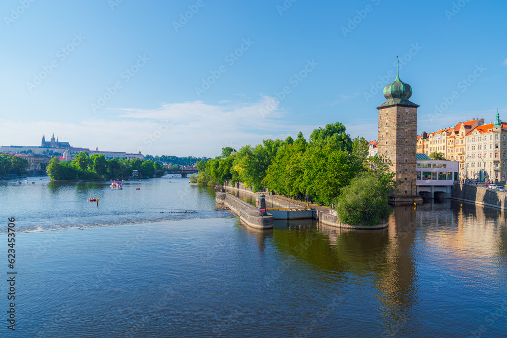 Fototapeta premium A tranquil scene of the Vltava River in Prague, Czech Republic, with boats gliding past the historic buildings lining the shore