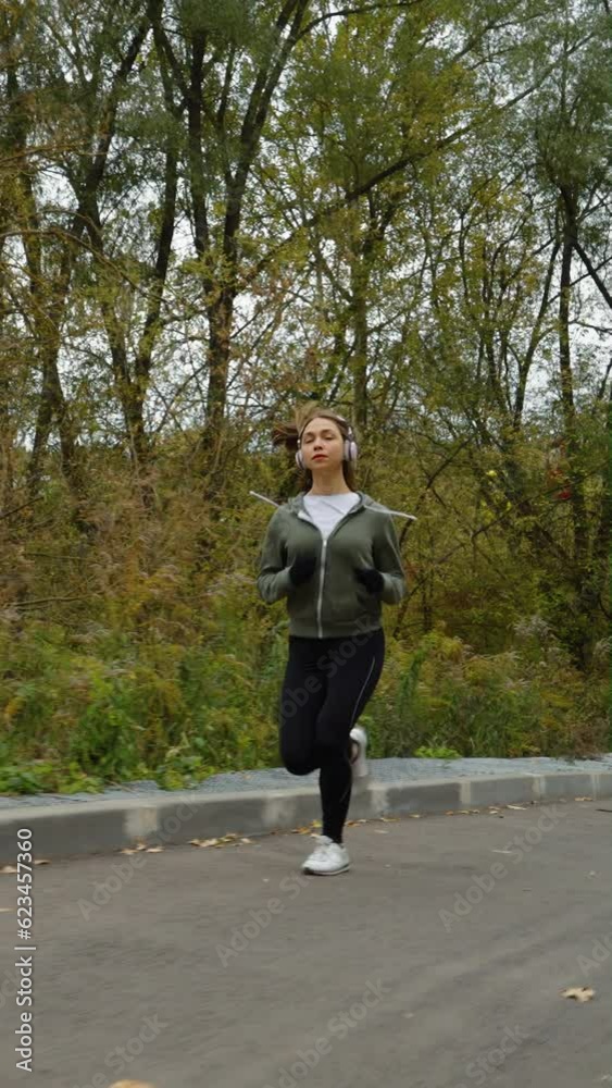 Vertical Screen: Slow motion female jogger running on road on autumn day, yellow trees on background. Tracking shot of active woman exercising outside. Concept of healthy lifestyle Vertical Screen: Slow motion female jogger running on road on autumn day, yellow trees on background. Tracking shot of active woman exercising outside. Concept of healthy lifestyle