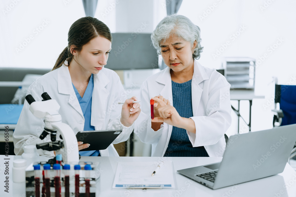 Two scientist or medical technician working, having a medical discuss meeting with an Asian senior female scientist supervisor in the laboratory with online reading, test samples and innovation Two scientist or medical technician working, having a medical discuss meeting with an Asian senior female scientist supervisor in the laboratory with online reading, test samples and innovation