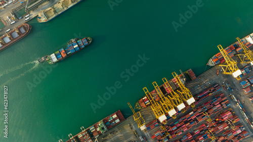 commercial port loading and unloading cargo from container ship import and export by crane for distributing goods by trailers transported to customers and dealers, aerial top view..