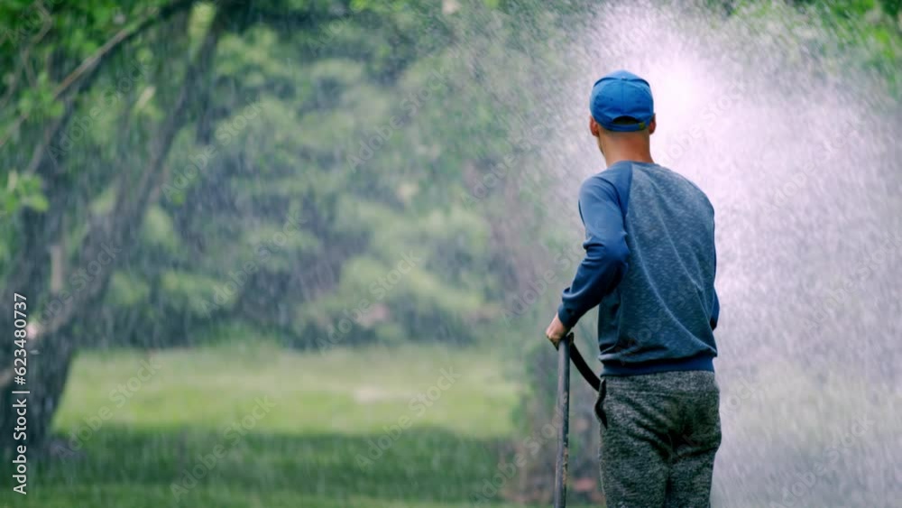 custom made wallpaper toronto digitalCity worker in regular clothing waters green lawn. Man sprays water on grass. Employee uses garden hose to water trees in city park