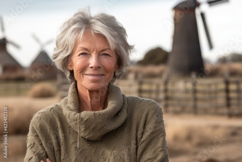 Environmental portrait photography of a satisfied mature girl wearing a cozy sweater against a rustic windmill background. With generative AI technology