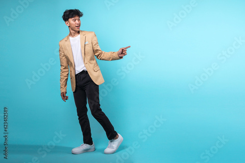 Full length of excited young man in semi formal clothes standing and pointing index fingers aside isolated on light blue background