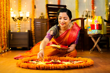 Happy traditional indian girl decorating Rangoli with flowers for diwali festival celebration on floor at home - concept of culture, custom and festive preparation.