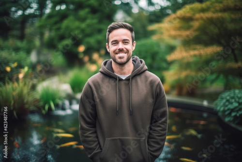 Three-quarter studio portrait photography of a happy boy in his 30s wearing a stylish hoodie against a tranquil koi pond background. With generative AI technology © Markus Schröder