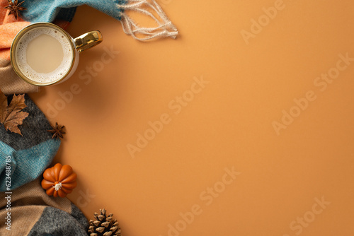 Set the autumn mood with this top view photo of a gilded cup of coffee, patchy scarf with pumpkin candles on brown isolated backdrop make it a perfect composition for text or advert placement