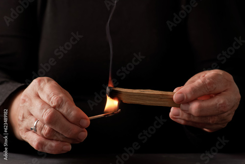 hands of a woman lighting a palo santo (holy stick) with a match with black background and copy space