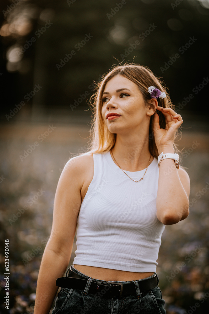 A young woman in a white shirt puts rye flowers behind her ear