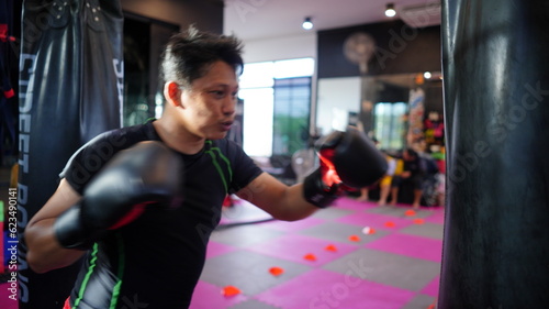 Thai boxing man in gym with sandbag. Athlete man in fitness with glove train in punching and kicking. Martial art exercise for strength. © soultkd