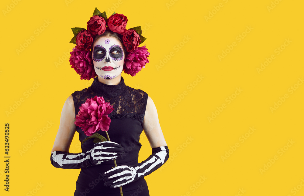 Zombie woman in stage halloween make-up holding red peony flower. Isolated on yellow background with copy space for any virtual object. Eyes gestures - pointing on recommend staff.