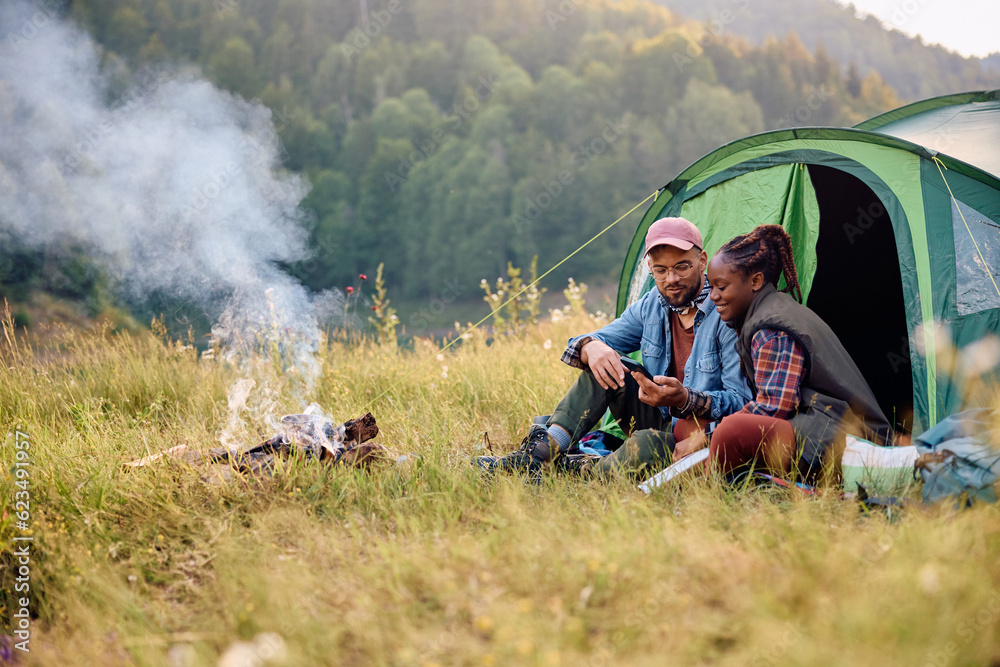 Happy couple using mobile phone while camping in nature.