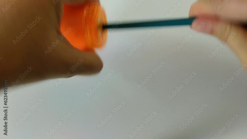 Un primer plano de unas manos de mujer afilando de forma manual un lápiz con una hoja blanca de fondo.