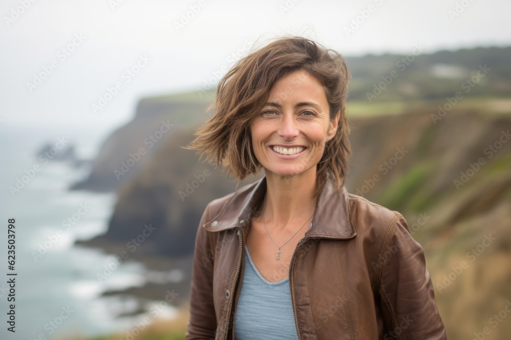 Headshot portrait photography of a grinning mature woman wearing a denim jacket against a scenic cliffside village background. With generative AI technology Headshot portrait photography of a grinning mature woman wearing a denim jacket against a scenic cliffside village background. With generative AI technology