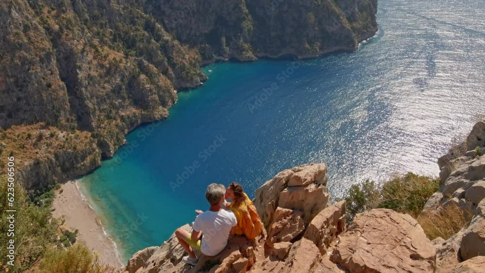 Aerial view of lovely couple sitting and kissing on edge of cliff over Butterfly valley high canyon Fethiye, Turkey. Popular and famous touristic point for tourists and travelers. traveling together
